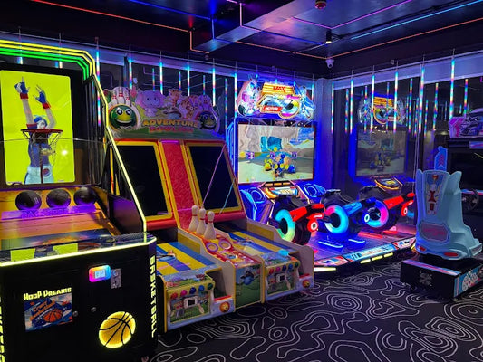 Arcade with various games like basketball, bowling, and racing, illuminated by colorful neon lights.