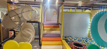 A colorful indoor playground with slides, a ball pit, and a target game for children.