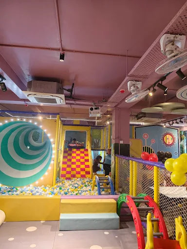 Children play in a colorful indoor playground with a ball pit and slides.