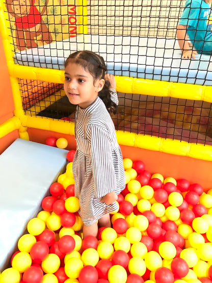 A young girl stands in a ball pit filled with red and yellow balls.