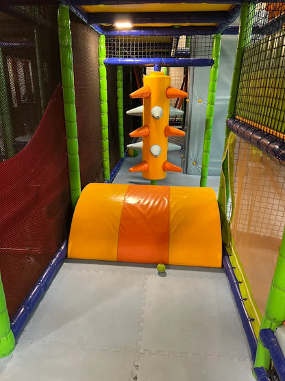 A colorful indoor playground with soft obstacles and a small yellow ball on the floor.
