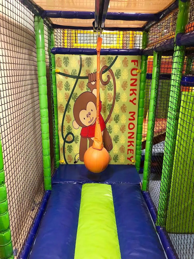 A colorful indoor playground with a monkey-themed backdrop and a soft landing area for children.