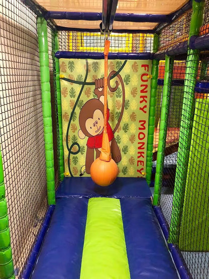 A colorful indoor playground with a monkey-themed backdrop and a soft landing area for children.