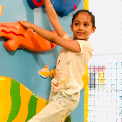 A young girl climbs on a colorful wall with fish decorations.