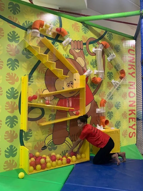 A young woman plays with balls in a colorful indoor playground with a monkey theme.