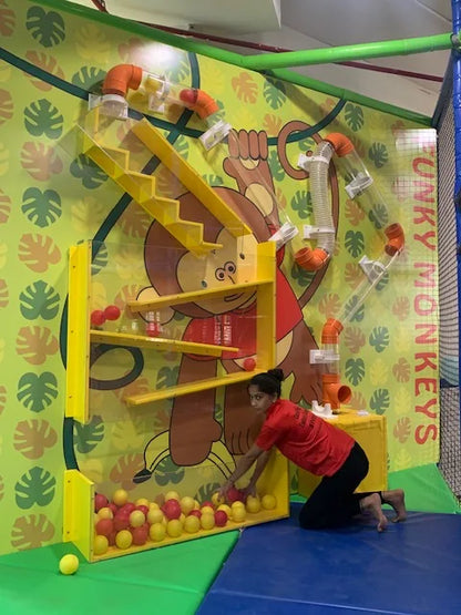 A young woman plays with balls in a colorful indoor playground with a monkey theme.