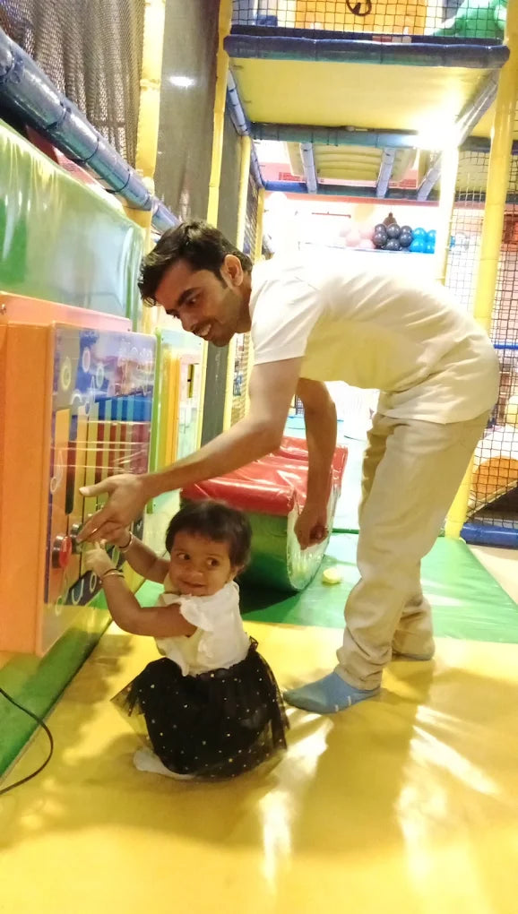 A father and toddler play with an interactive toy panel in a colorful indoor playground.