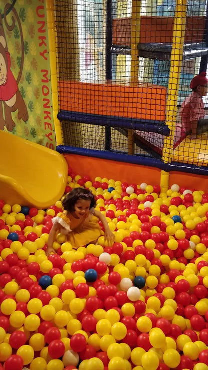 A young child plays in a ball pit next to a yellow slide in an indoor playground.