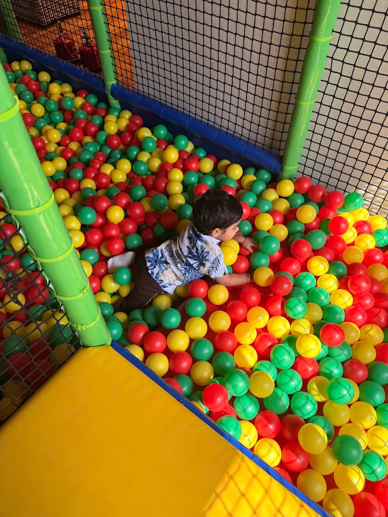 A young child plays in a ball pit filled with red, yellow, and green balls.