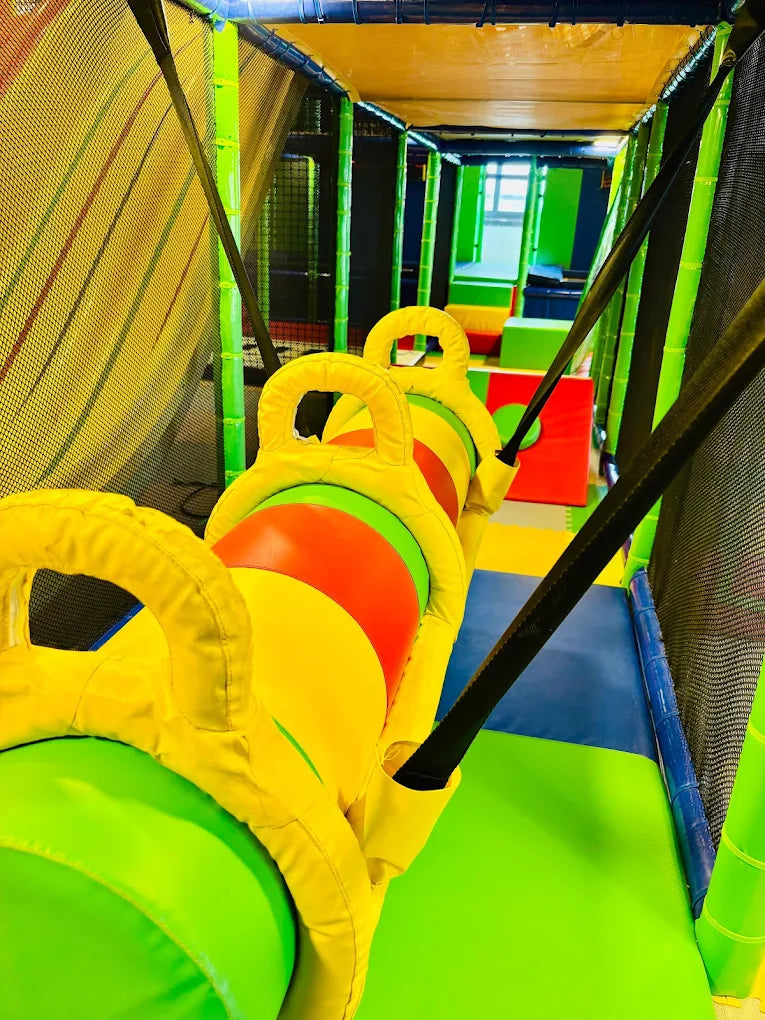 A colorful indoor playground with soft, padded obstacles and tunnels for children. The image shows a bright and engaging play area designed for active fun.