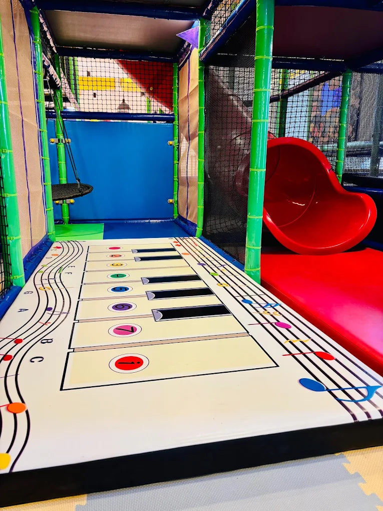 A colorful indoor playground with a giant floor piano and a red slide.