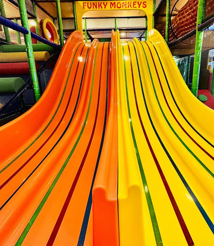 A bright indoor playground with two colorful slides, orange and yellow, for children.