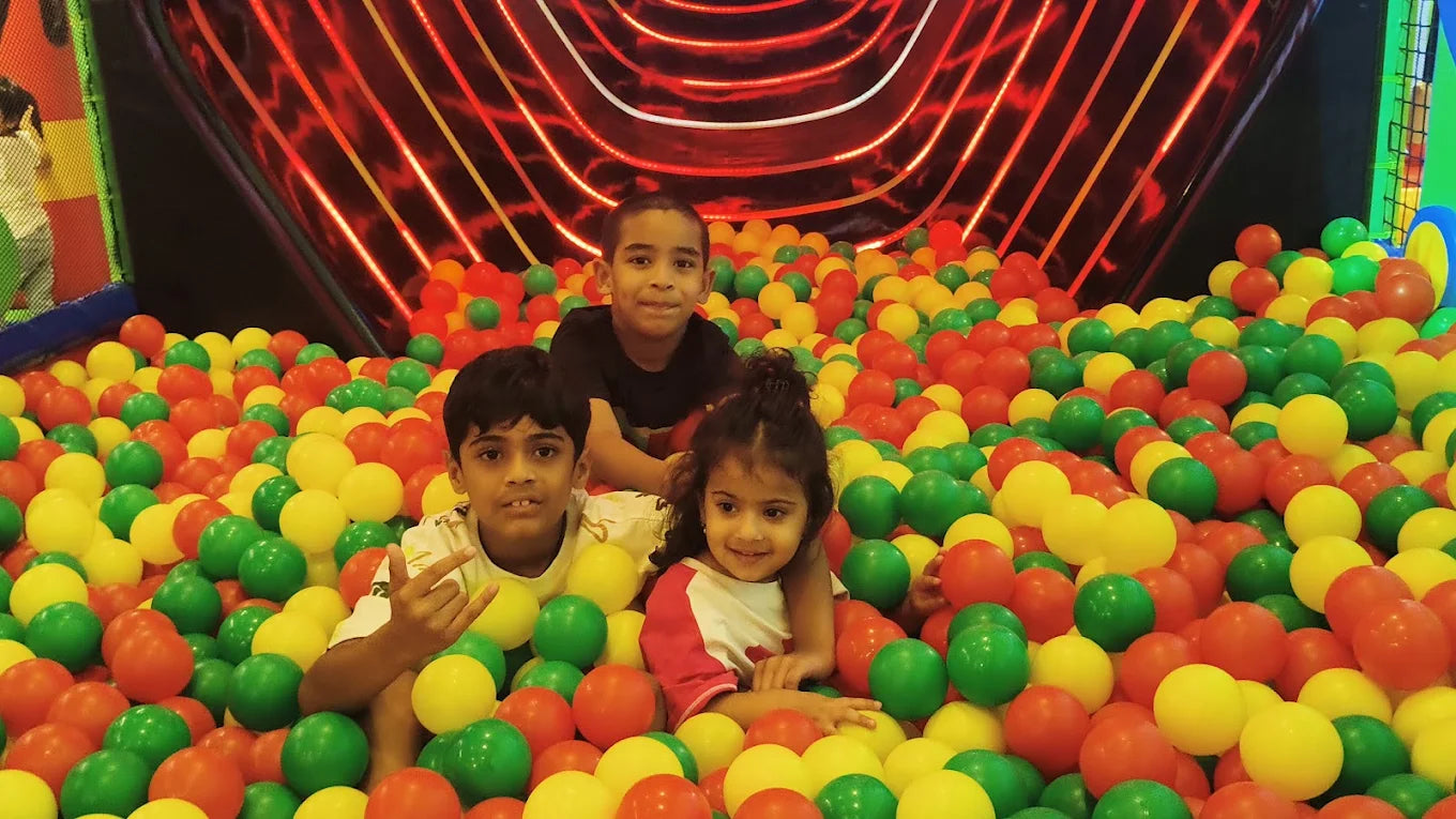 Three young children smile while playing in a colorful ball pit.