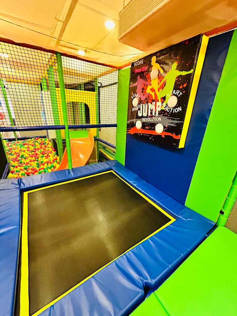 A colorful indoor playground with a trampoline, ball pit, and a "Jump Revolution" game for children.
