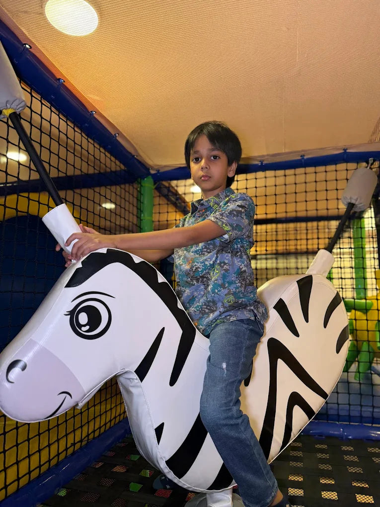 A young boy rides an inflatable zebra in a colorful indoor play area.