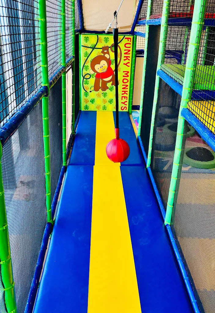 A colorful indoor playground with a monkey-themed banner and a red ball hanging from a rope.