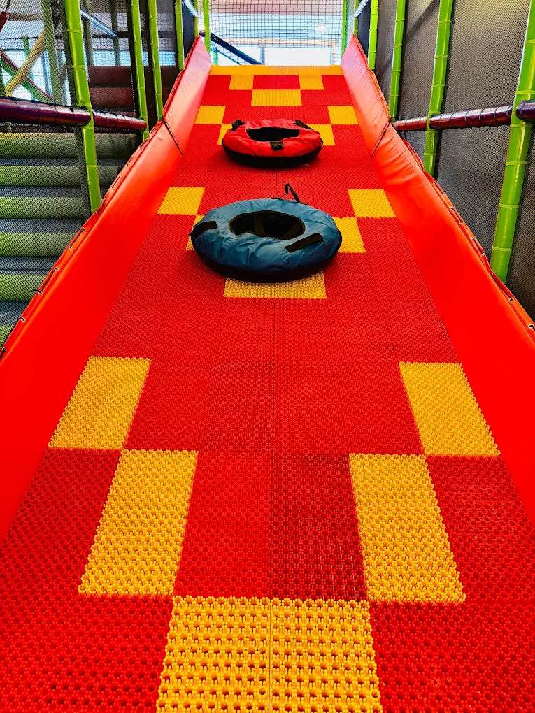 Two inflatable tubes sit on a red and yellow checkered slide in a children's play area.