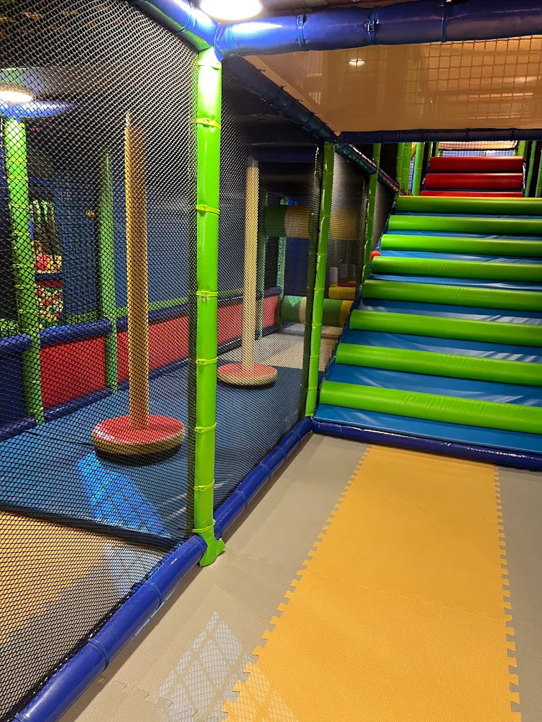 A colorful indoor playground with soft mats, netting, and a large slide.
