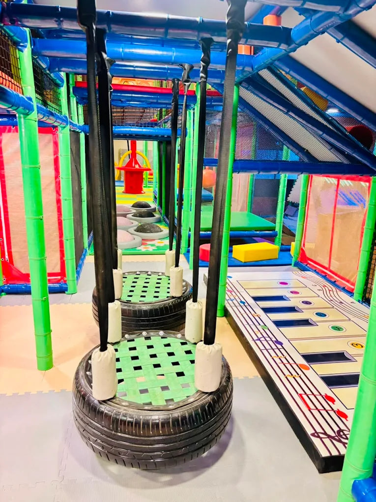 Children's indoor playground with tire swings and a giant piano mat.