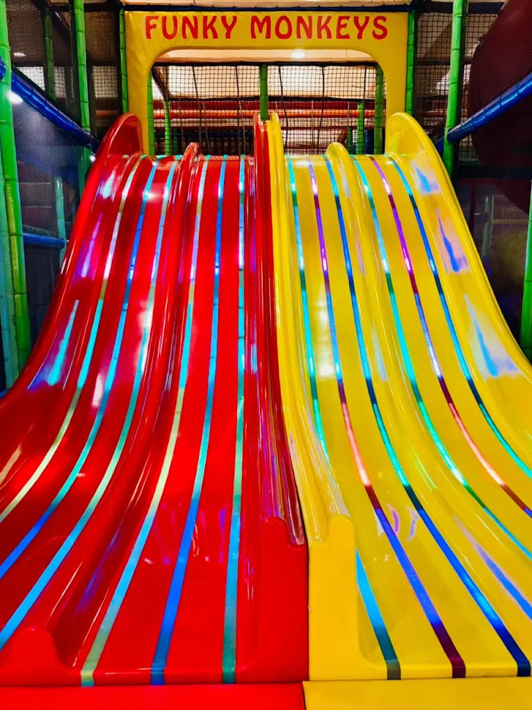 Two colorful slides, red and yellow, in a children's play area.