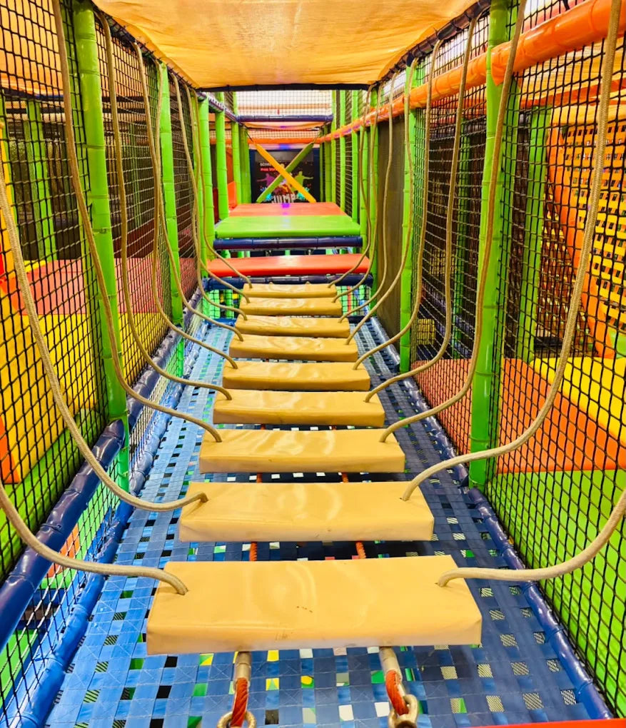 A suspended rope bridge with wooden planks in a colorful indoor playground for children.