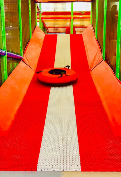 A child slides down a red and white tube slide in a colorful indoor playground.