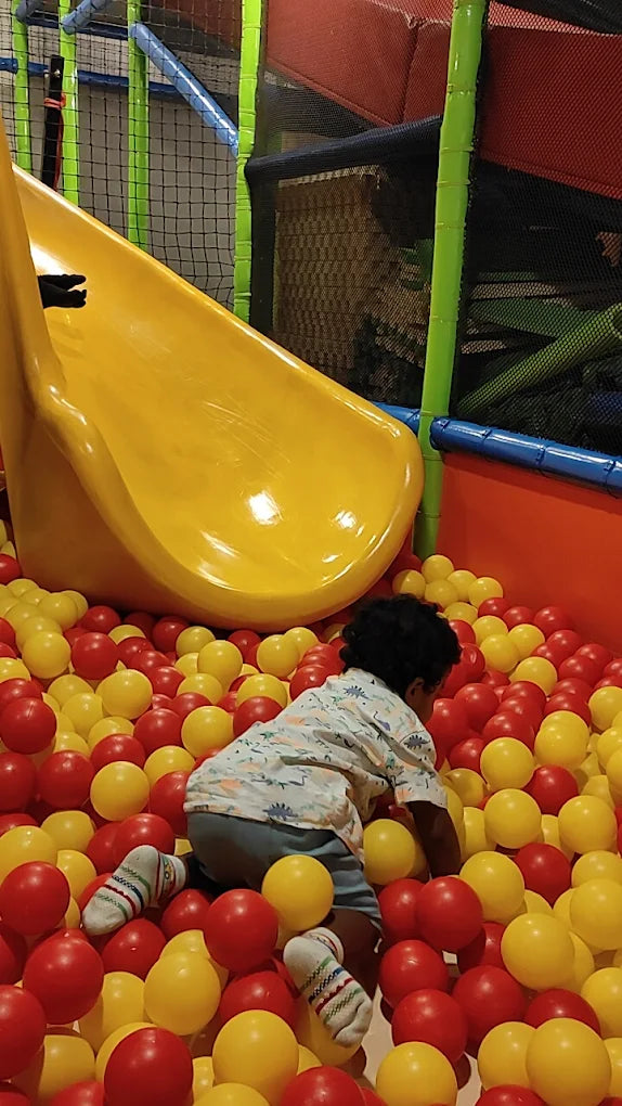 A young child plays in a ball pit with a yellow slide.