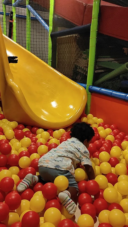 A young child plays in a ball pit with a yellow slide.