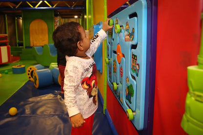A young child plays with a colorful activity board in a brightly lit indoor playground.