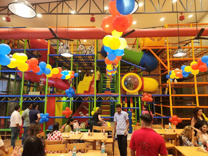 A colorful indoor playground with children and adults enjoying the space, decorated with balloons.