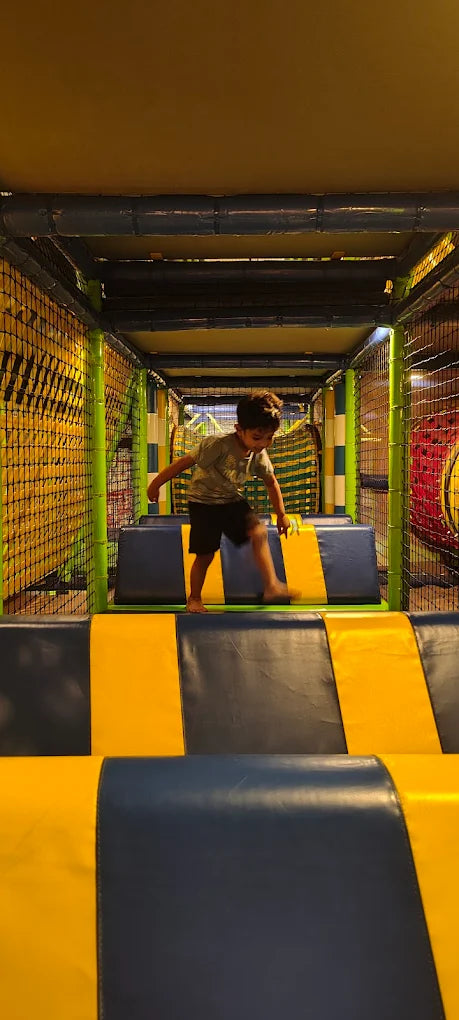 A young boy jumps across padded obstacles in a colorful indoor playground.