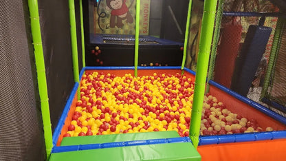 A ball pit filled with red and yellow balls, with a trampoline in the background.