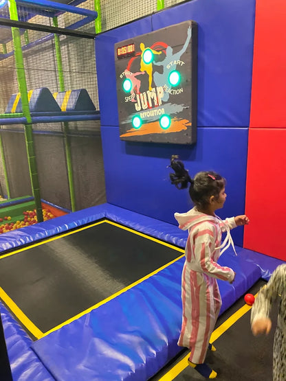 A young girl in a striped outfit jumps on a trampoline next to a "Jump Revolution" game.