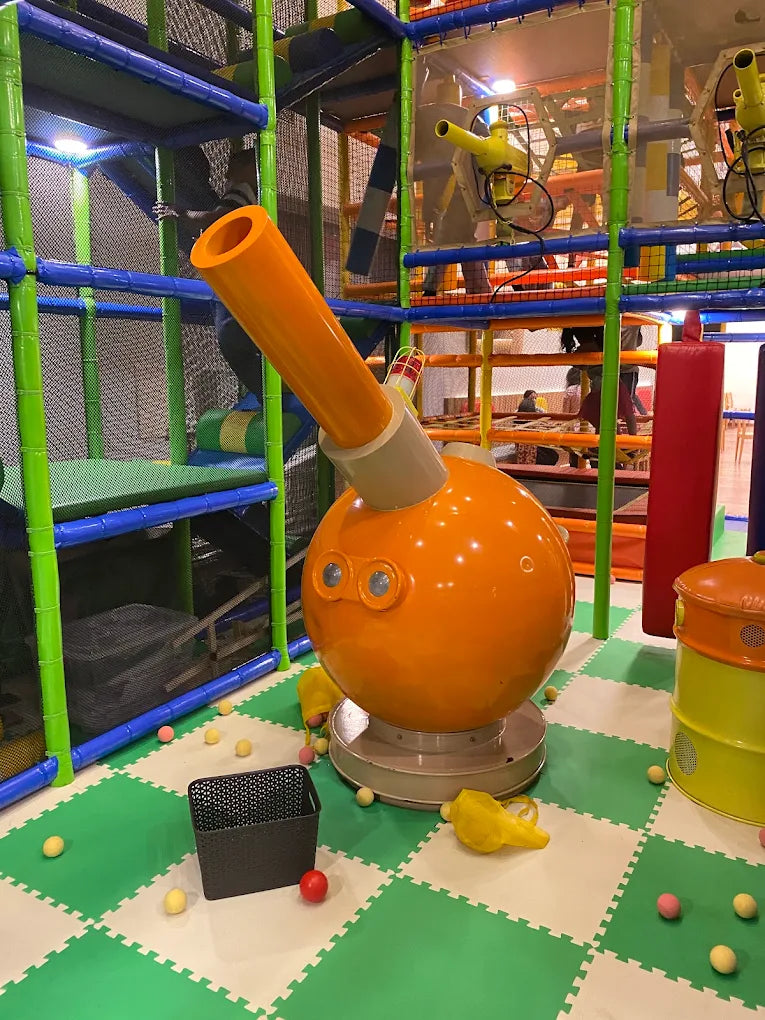 A large orange cannon-like toy in a colorful indoor playground with children playing.