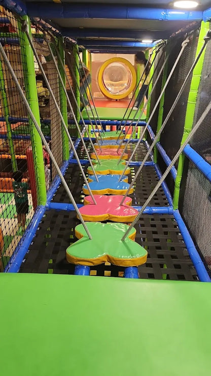 A colorful indoor playground with a rope bridge and children playing.