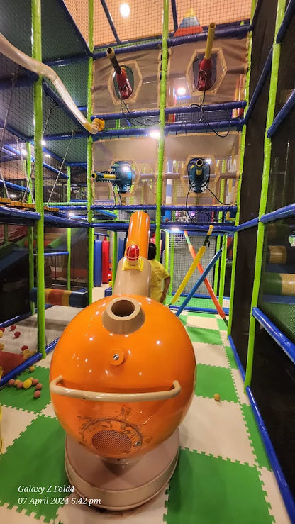 An indoor playground with a large orange ball structure and a child playing.