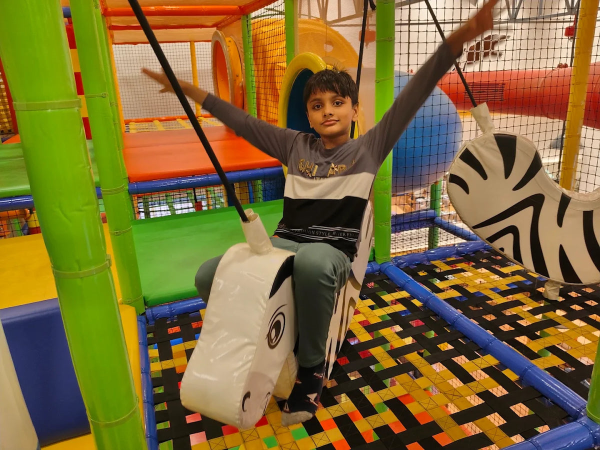 A young boy swings on a zebra-shaped ride in a colorful indoor playground.