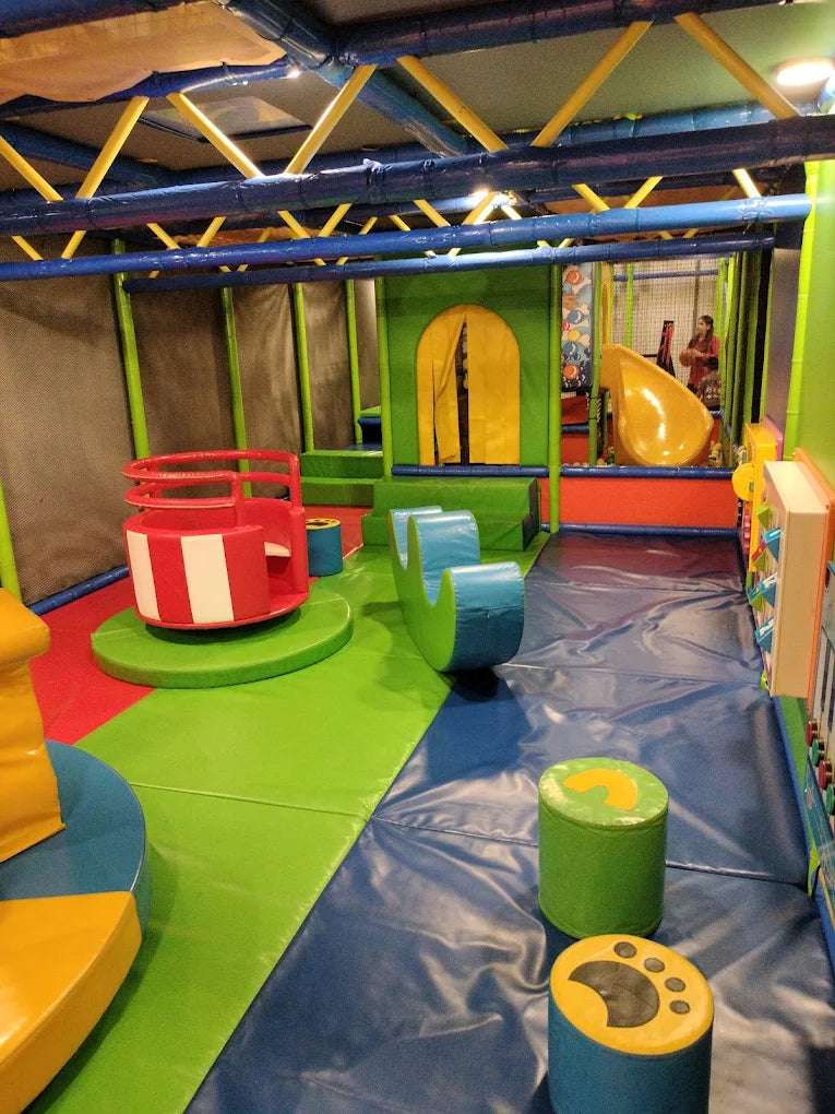 A colorful indoor playground with slides, soft play structures, and children playing.