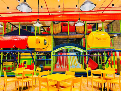 A colorful indoor playground with slides and tunnels, featuring yellow tables and chairs for children.