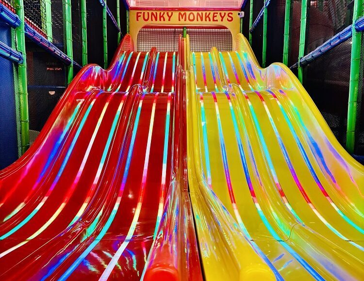A colorful indoor playground slide with red and yellow lanes, featuring lights.