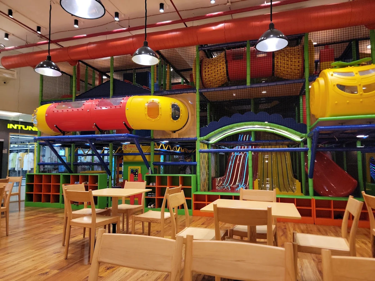 A colorful indoor playground with slides and tunnels, and a seating area for children.