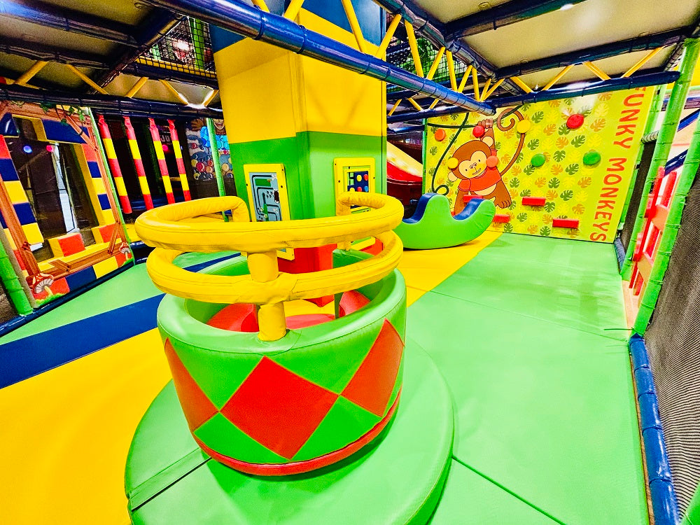 A colorful indoor playground with climbing structures and a monkey-themed wall.