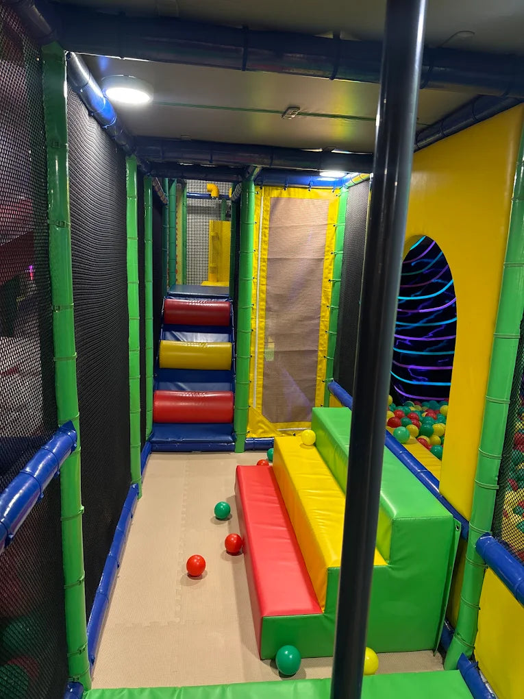 A colorful indoor playground with soft play structures and a ball pit for children.