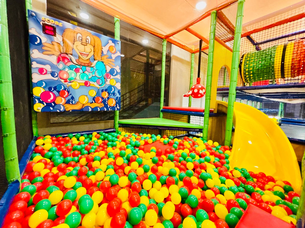 A colorful ball pit with a yellow slide and a cartoon dog game, likely in a children's play area.