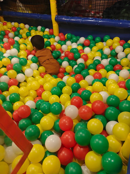 A young child plays in a ball pit filled with red, yellow, and green balls.