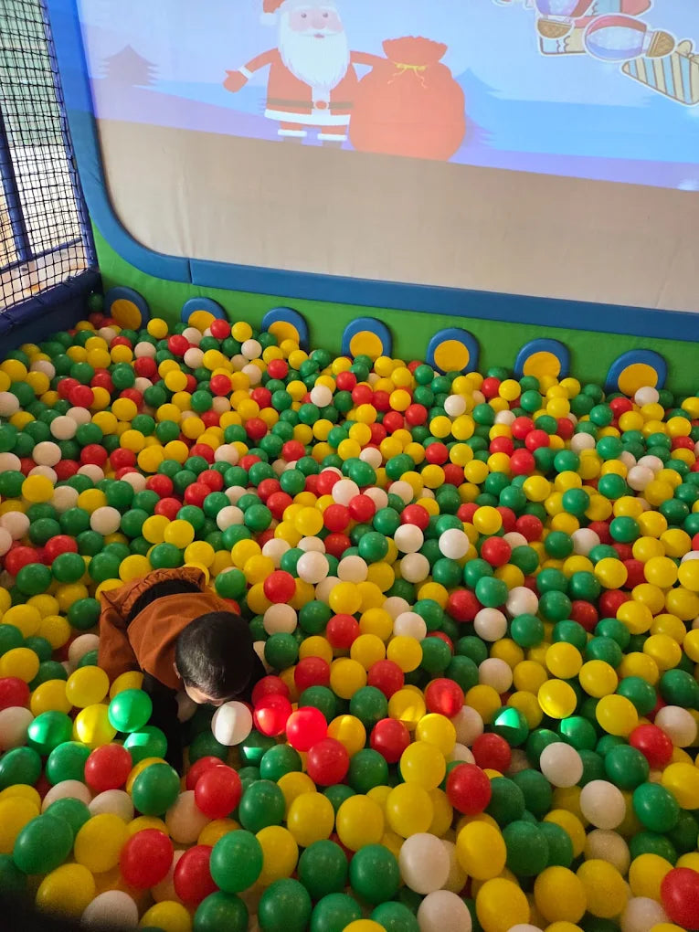 A child plays in a ball pit with a Christmas projection above.