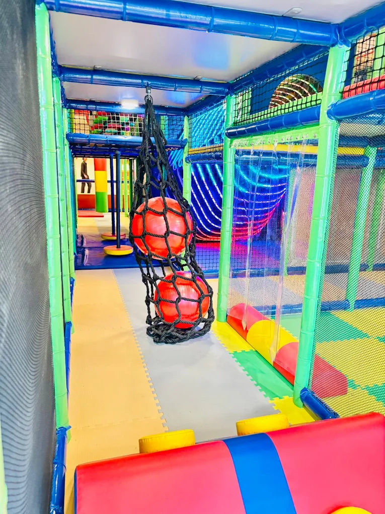 A colorful indoor playground with soft flooring and hanging red balls.