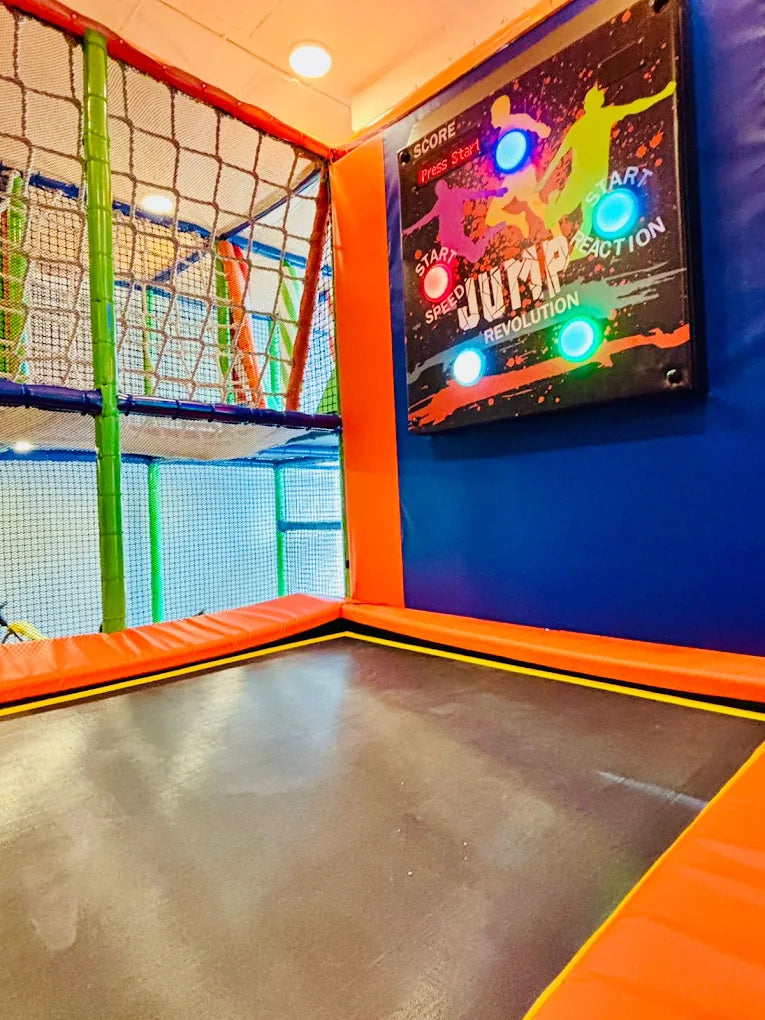 A trampoline park with a "Jump Revolution" game board and colorful netting.