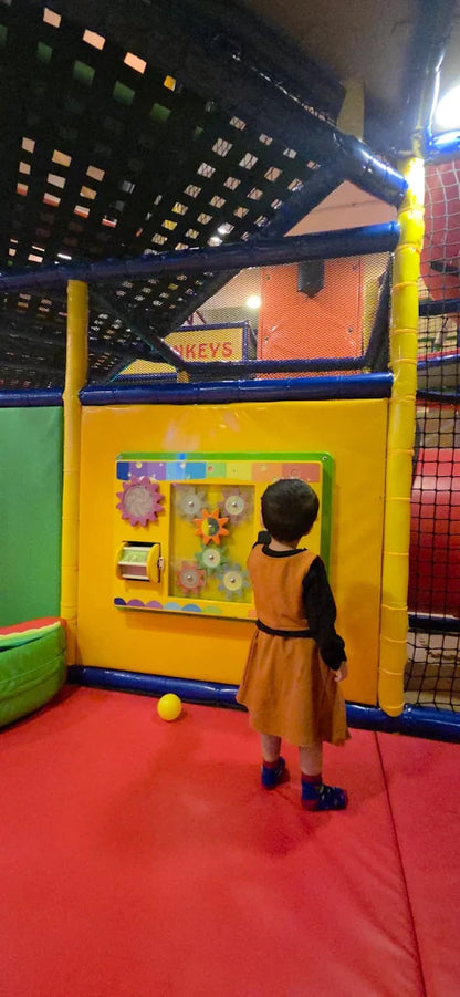 A young child plays with a gear wall in a colorful indoor playground.