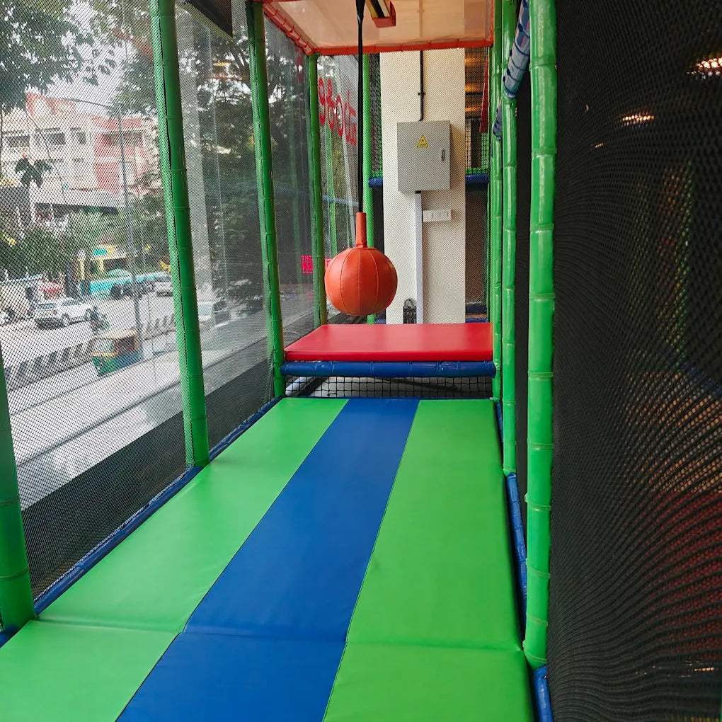 An indoor playground with padded green and blue mats, a red platform, and an orange punching bag.